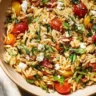 A vibrant bowl of Lemon Basil Pasta Salad with fresh ingredients and herbs.