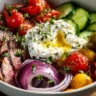 Mediterranean steak bowl topped with fresh vegetables and herbs