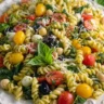 Delicious pesto pasta salad served in a bowl with cherry tomatoes and basil.