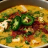 Bowl of spicy jalapeño popper chicken soup garnished with cheese and jalapeños